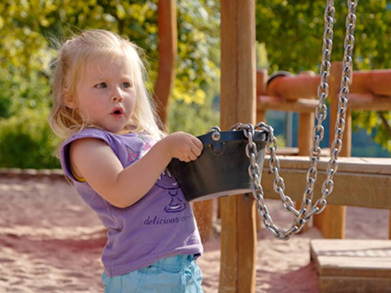 Ein Mädchen spielt mit einem Sandeimer auf dem Spielplatz.