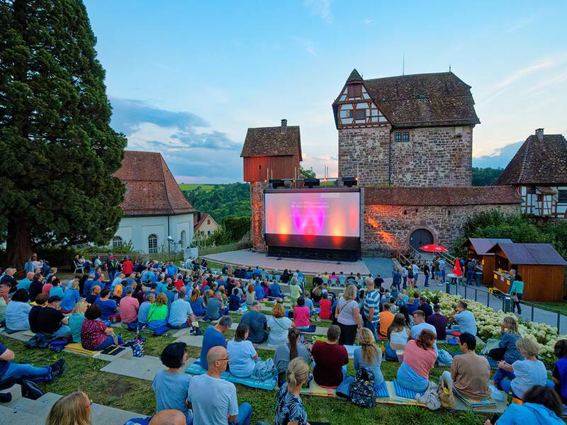 Voll besetzter Schlossgarten beim Kino im Schlossgarten in der Abenddämmerung vor Filmbeginn.