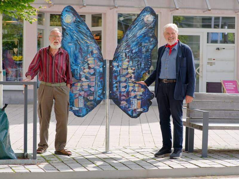 Heinrich Wille und Wolfram Paul stehen neben dem von Wolfram Paul gestalteten Holzschmetterling auf dem Marktplatz.