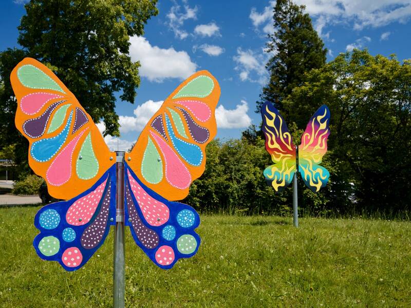 Zwei sommerlich bunt bemalte Holzschmetterlinge auf einer Wiese.