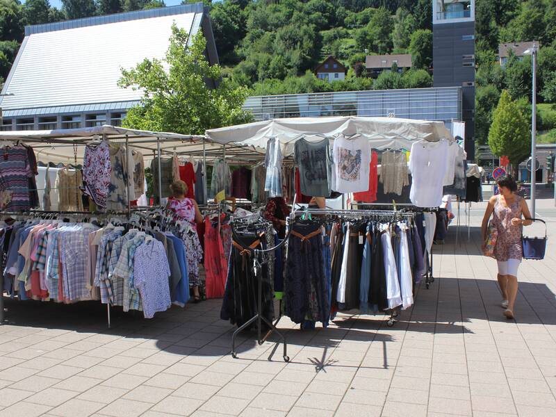 Eine Frau bummelt auf dem Marktplatz an einem Krämermarkt-Stand mit Klamotten vorbei.