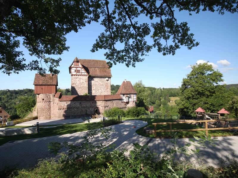 Das Altensteiger Schloss vom oberen Ende des Schlossgartens aufgenommen mit herabhängenden Ästen am oberen Bildrand.